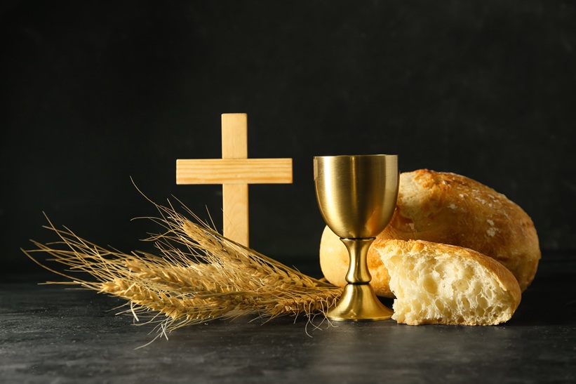 Cup of wine with bread and cross on dark background